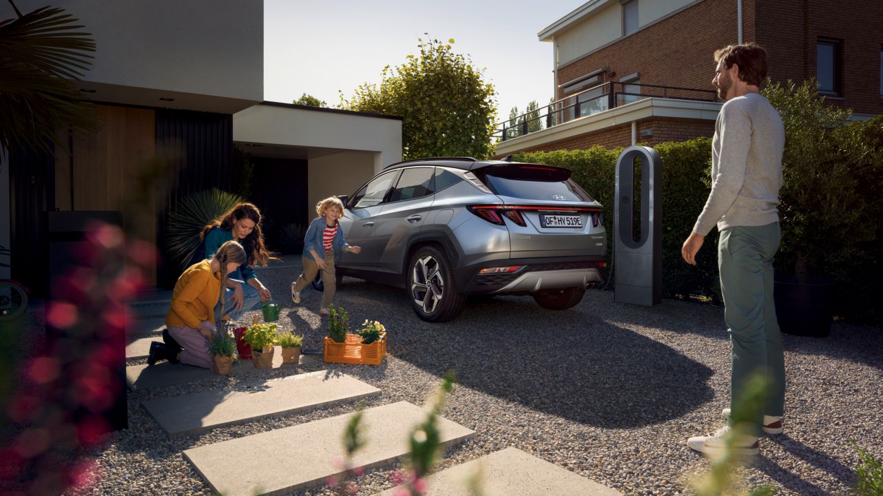 Zcela nové kompaktní SUV Hyundai TUCSON Plug-in Hybrid, zaparkované před domem s dětmi.